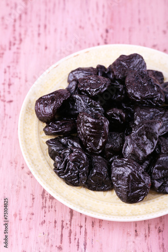 Plate with heap of prunes on color wooden background