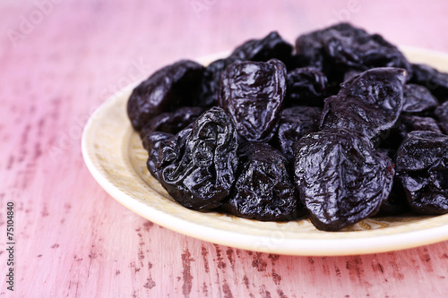 Plate with heap of prunes on color wooden background