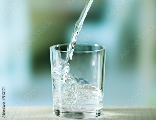 Pouring water from bottle on glass on light background