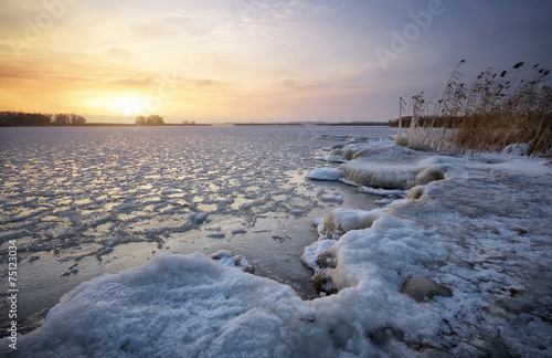 Beautiful winter landscape with frozen lake and sunset sky. © es0lex