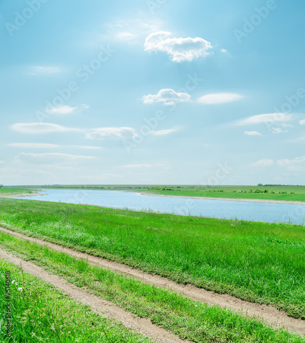 sunny sky with clouds and green landscape with river and road