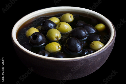 Ceramic rustic bowl of black and green olives on black surface.