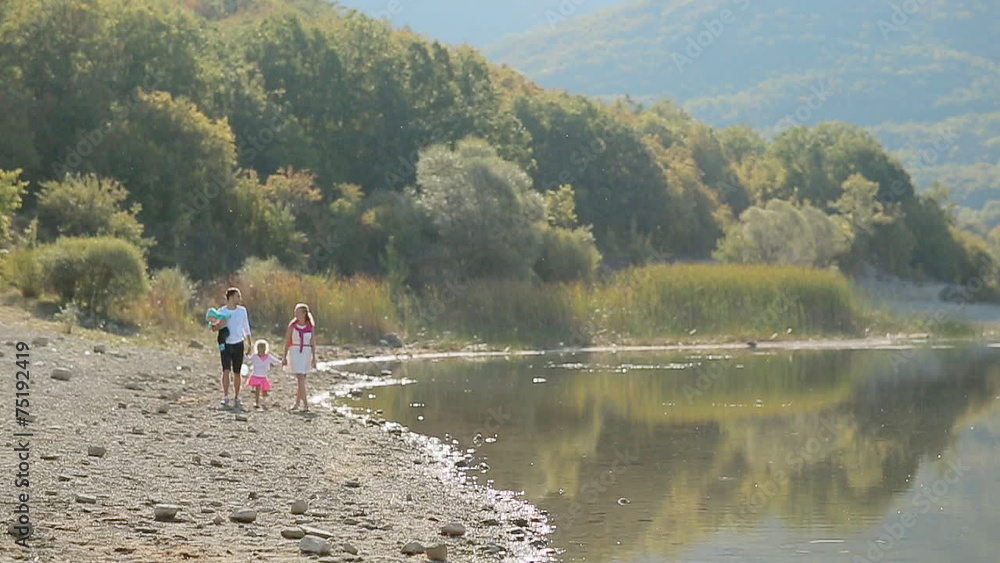 Happy family with two young daughters walking along the lake in Happy family with two young daughters walking along the lake in