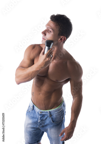 Muscular man shirtless using electric shaver, looking away