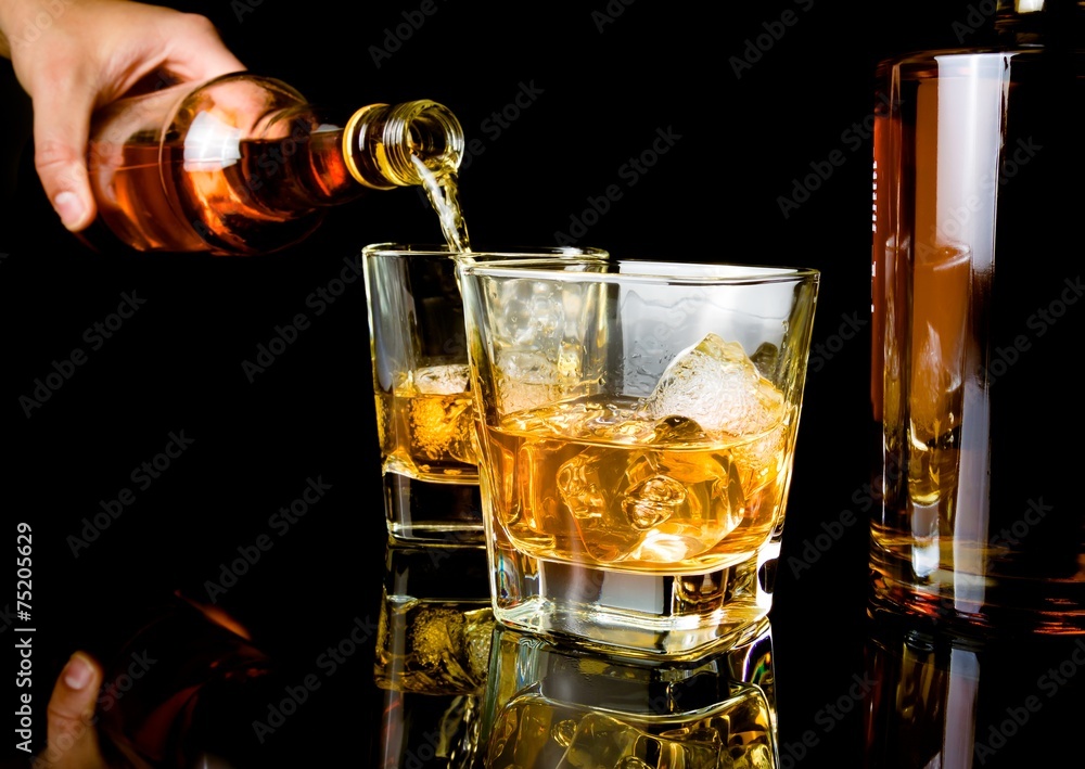 barman pouring whiskey in front of whiskey glass and bottles