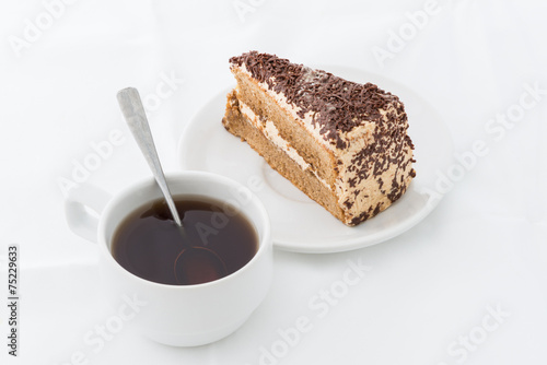 Chocolate cake slice with curl on white dish with hot drink