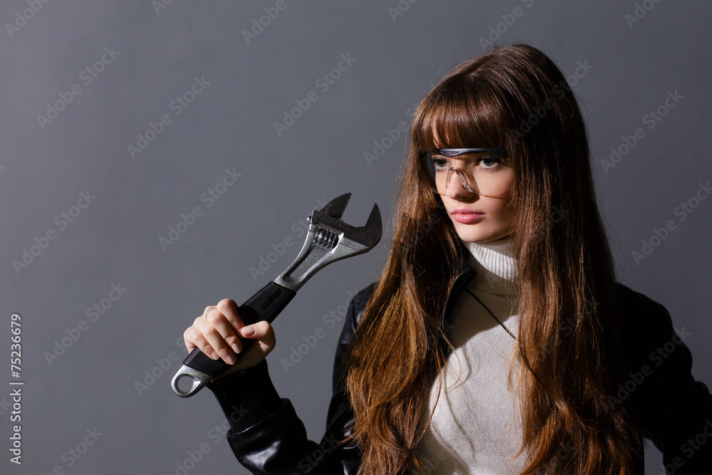 Girl in protective glasses with adjustable wrench on a dark back Girl in protective glasses with adjustable wrench on a dark back