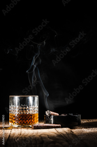 Glass of alcohol and smoking noble cigar on a black background