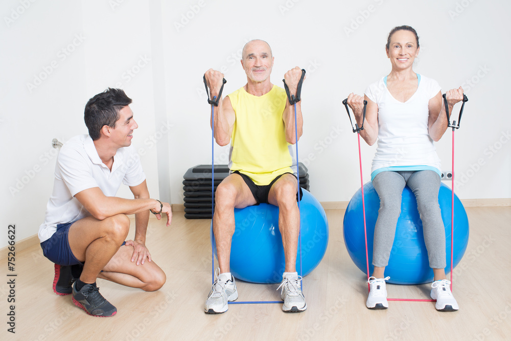 Obraz premium Zwei Senioren beim Seiltraining auf Fitnessball mit Trainer