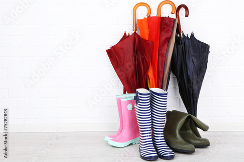 Bright umbrellas leaning against a bricks wall and gumboots