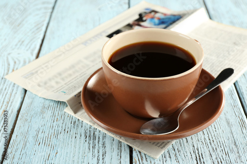 Cup of coffee with newspaper on color wooden background