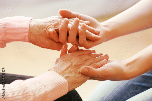 Old and young holding hands on light background, closeup