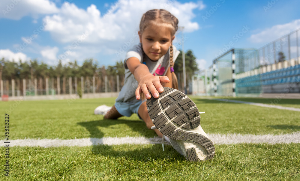 young girl stretching legs on soccer field at sunny day young girl stretching legs on soccer field at sunny day