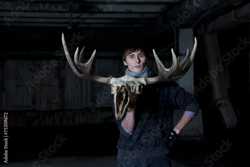 young man with a deer skull with horns in a dark basement