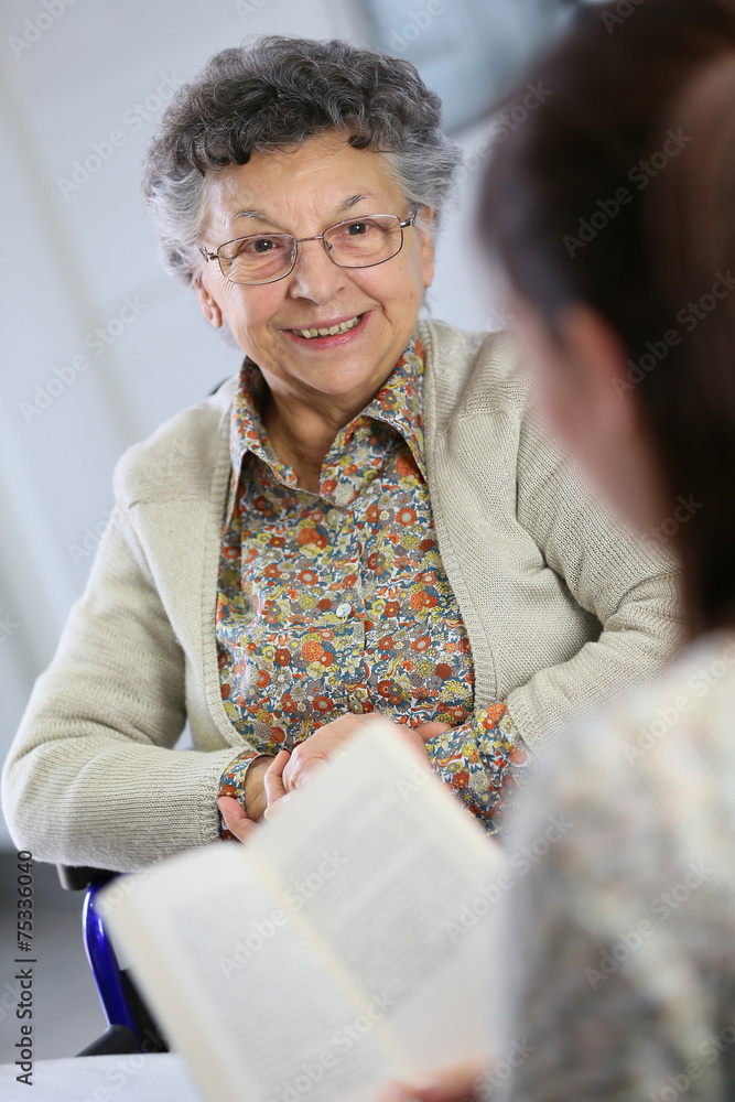 Homec arer reading book to old woman in nursing home