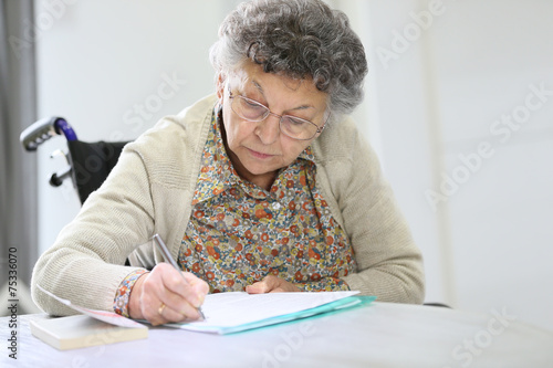 фотографія Elderly woman in wheelchair filling up medical form