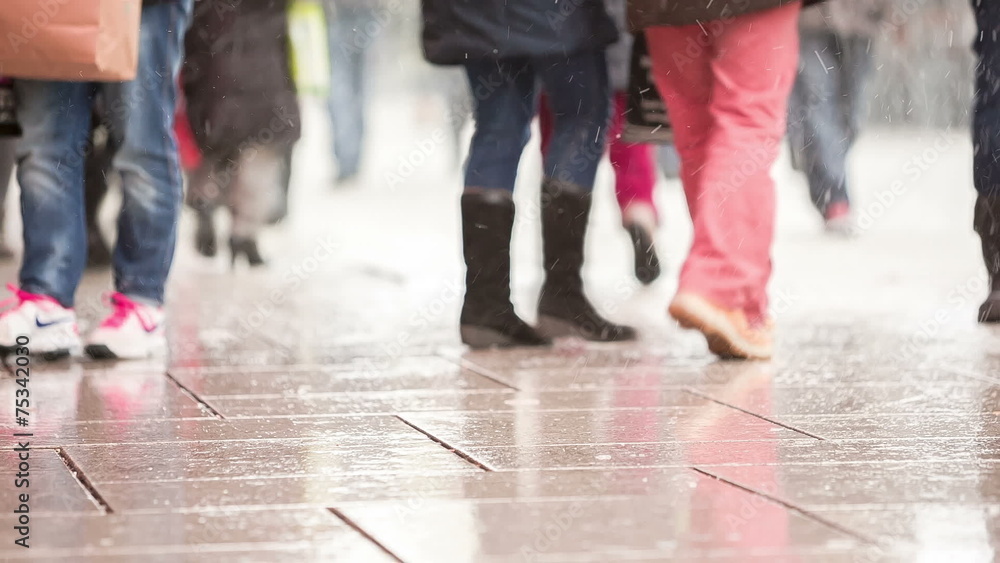 Legs of people walking on wet tiled street with snowfall Legs of people walking on wet tiled street with snowfall
