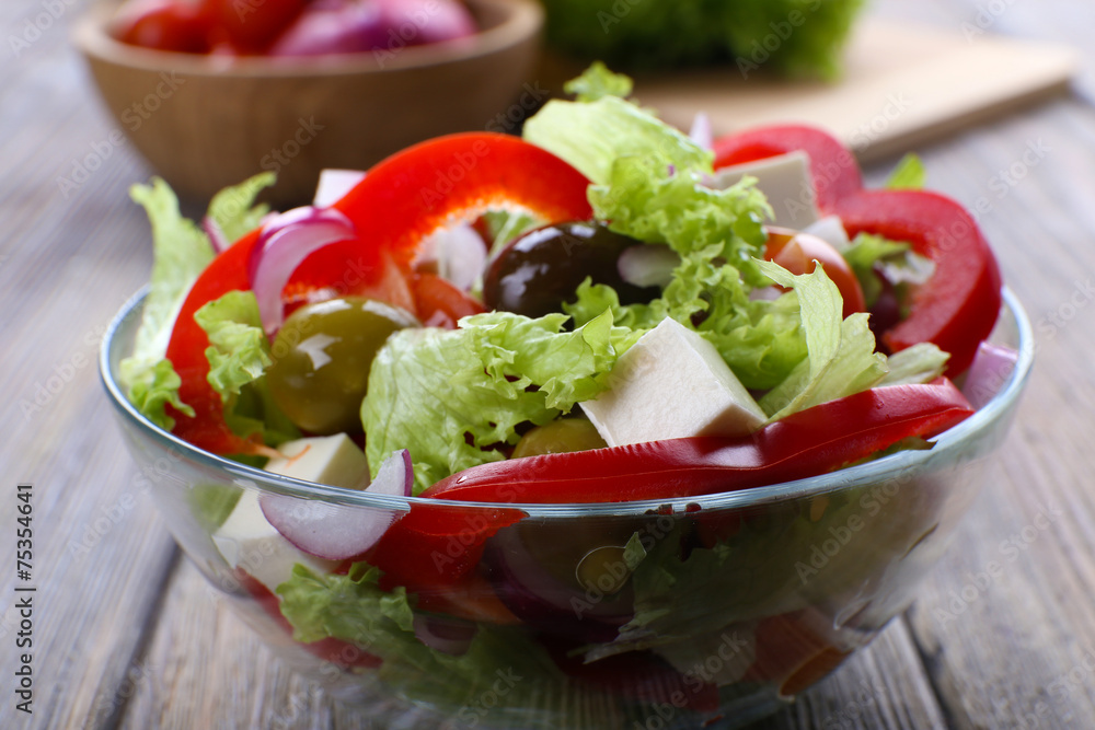 Greek salad in glass dish on wooden table background Greek salad in glass dish on wooden table background