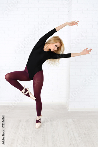 Beautiful young ballerina on wall background