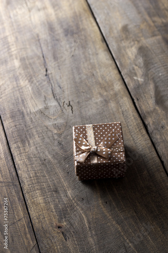 Gift box with ribbon ornament on wooden background.