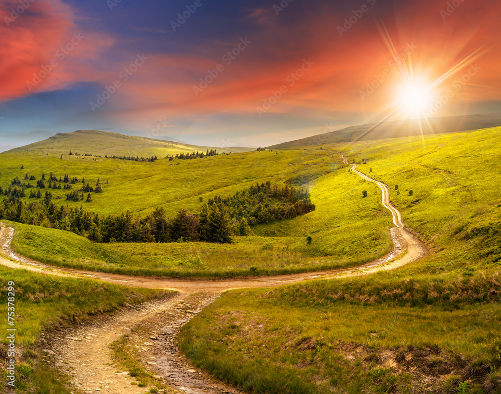 Obraz premium cross road on hillside meadow in mountain at sunrise at sunset