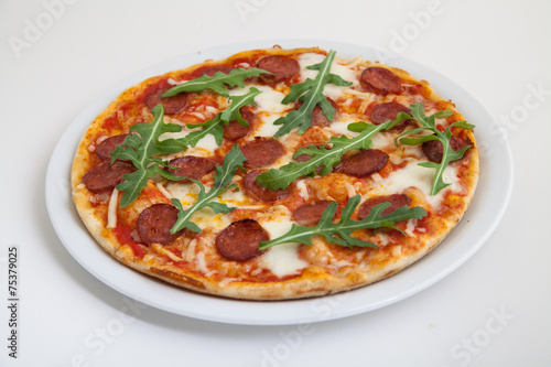 pizza with salami, cheese and arugula on white plate