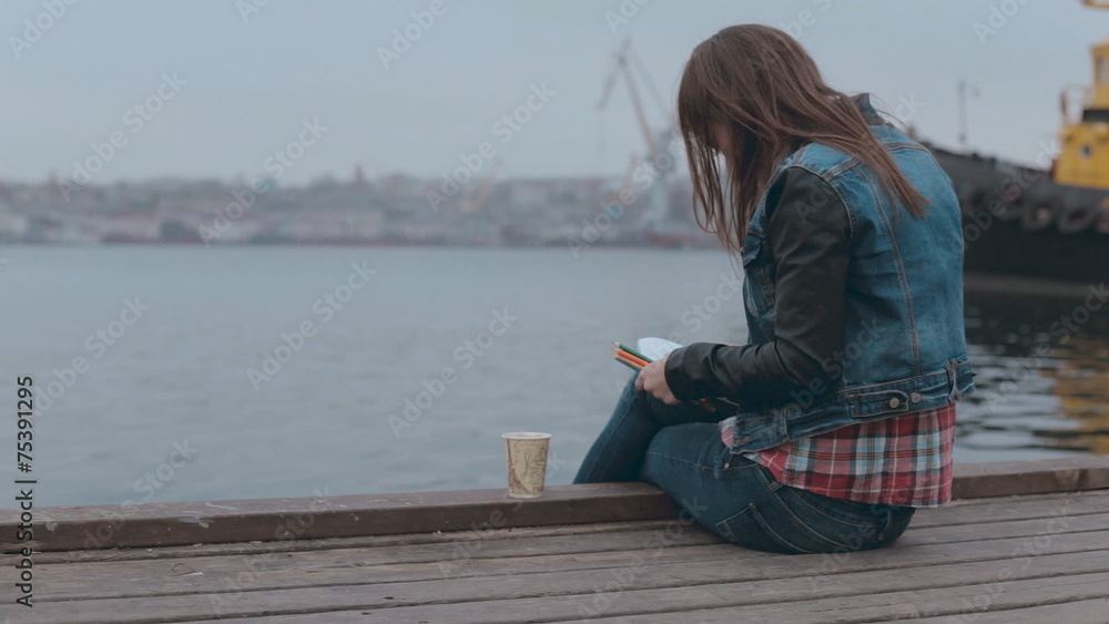 Absorbed in drawing girl sitting on a wooden pier near the sea Absorbed in drawing girl sitting on a wooden pier near the sea
