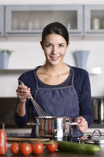 Glückliche junge Hausfrau kocht Essen photo