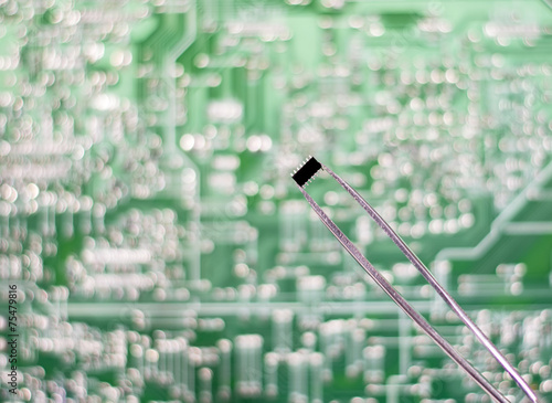 The chip in the tweezers on the circuit Board background