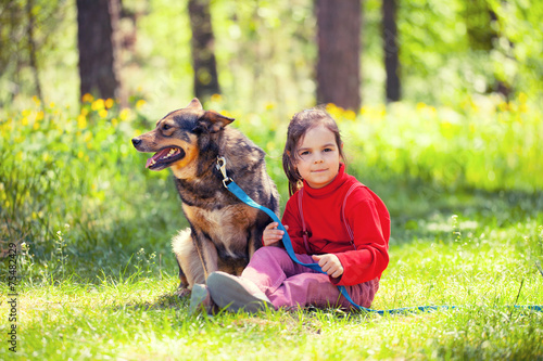 Happy little girl with big dog sitting on green lawn