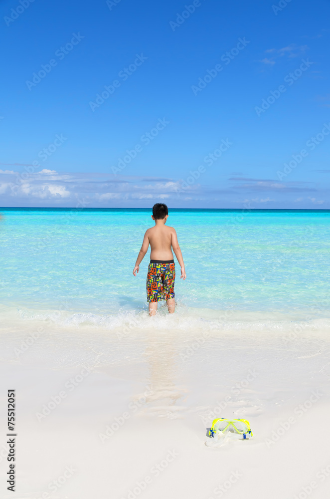 Back view of a little Asian boy heading towards blue tropical se