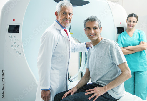 Obraz na płótnie Man in 40s ready to undergo MRI scan, assisted by two smiling do