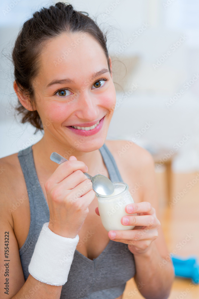 Attractive sportive woman eating yoghurt after sport - obrazy, fototapety, plakaty 
