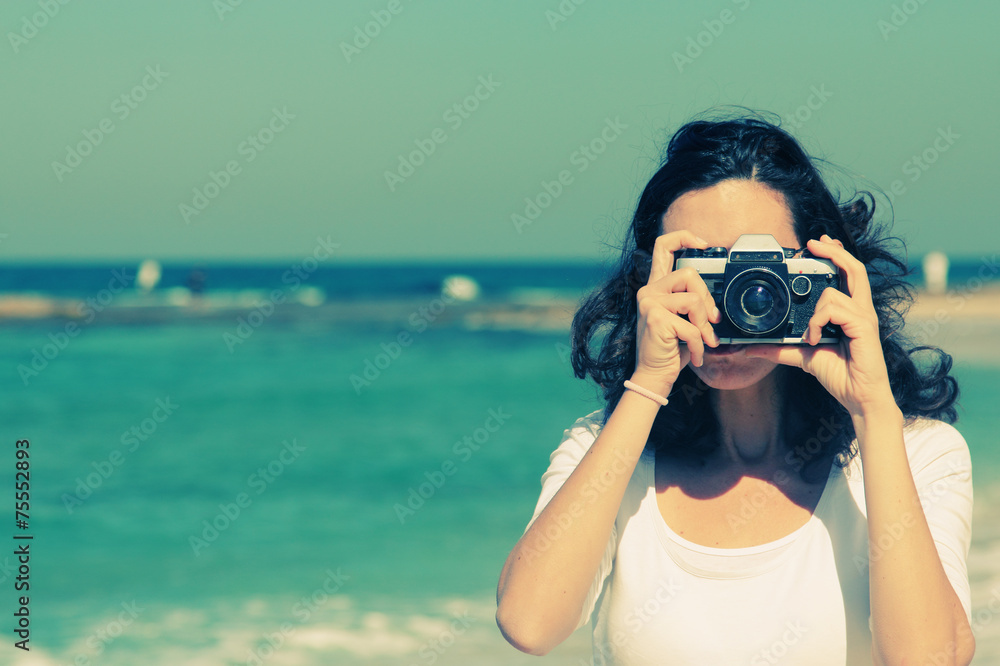 Woman with vintage retro camera having fun on the beach on blue