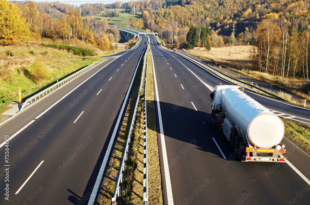 The highway between deciduous trees in autumn colors, white tank
