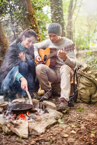  a couple sitting near a campfire, he plays guitar