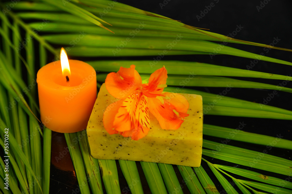 candle and orange orchid on green palm texture on black