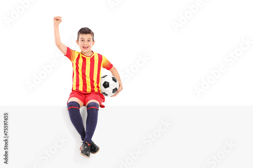 Fototapeta Naklejka Na Ścianę i Meble -  Junior soccer player gesturing joy seated on panel