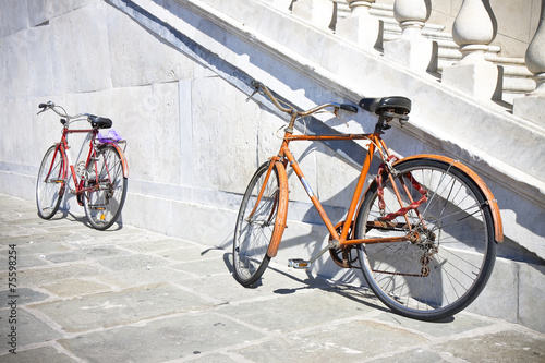 Two old rusty bicycles against a marble wall (Tuscany - Italy)