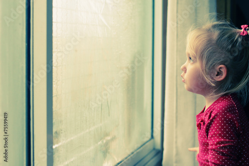 Cute 4 years old girl looking through the window