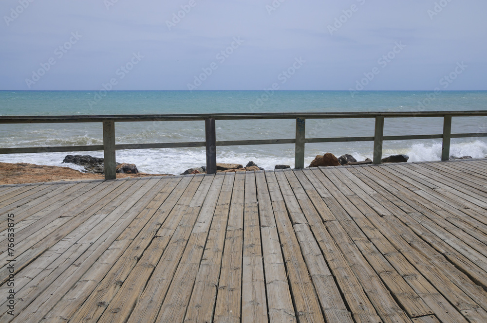 Wood boardwalk and railing by azure blue Mediterranean sea and c Wood boardwalk and railing by azure blue Mediterranean sea and c