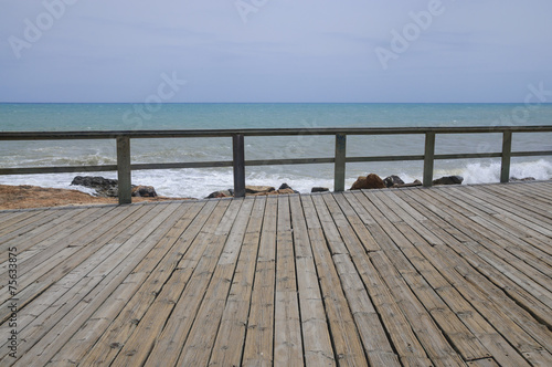 Wood boardwalk and railing by azure blue Mediterranean sea and c