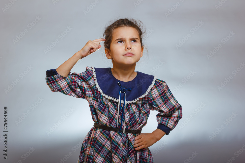 girl child thinks finger to head on a gray background girl child thinks finger to head on a gray background