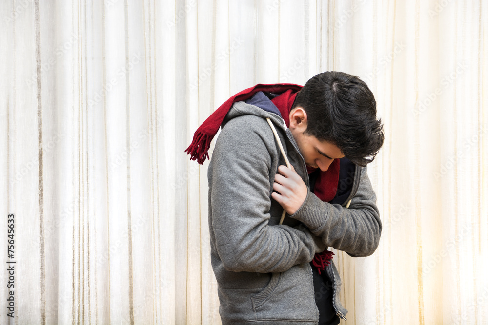 Young man feeling very cold, wearing heavy sweater and scarf Young man feeling very cold, wearing heavy sweater and scarf