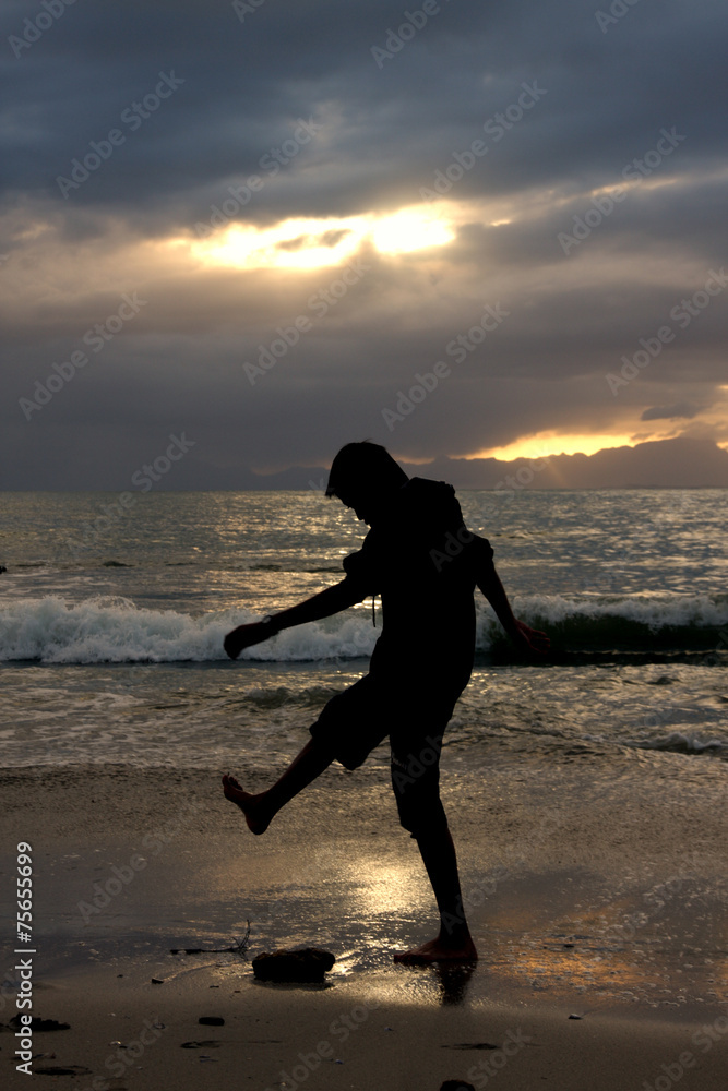Silhouette photo of a boy playing on a beach at golden hour. 