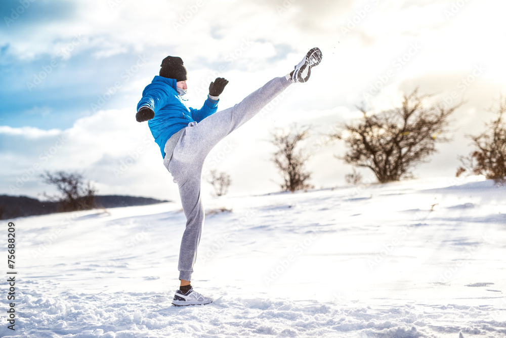 Man practicing a kick shot outdoor in snow. Fitness training