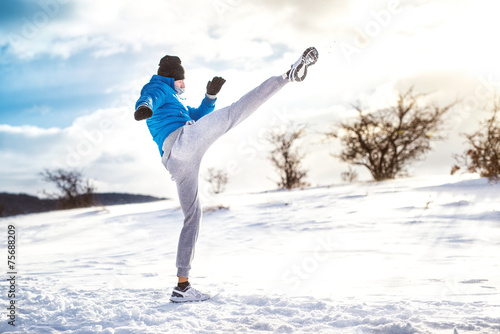 Man practicing a kick shot outdoor in snow. Fitness training © aboutmomentsimages
