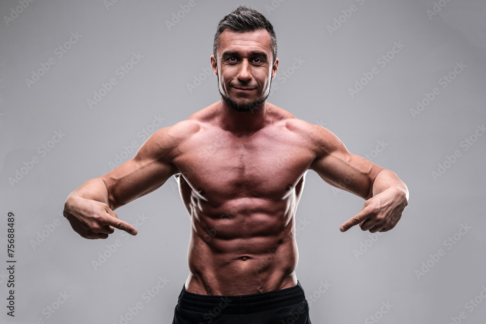 Fototapeta premium Handsome muscular man pointing at his abs over gray background