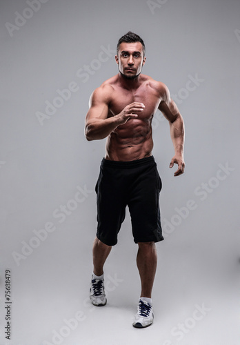 Portrait of a muscular man running over gray background