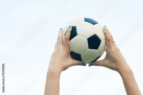 Woman holding a soccer ball up into the sky background